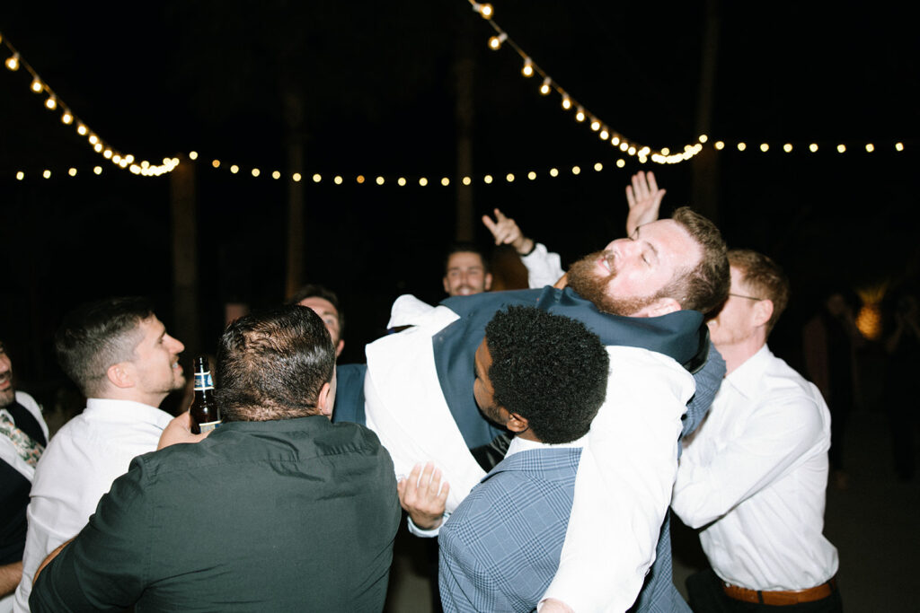 Guests picking groom up in the air at reception